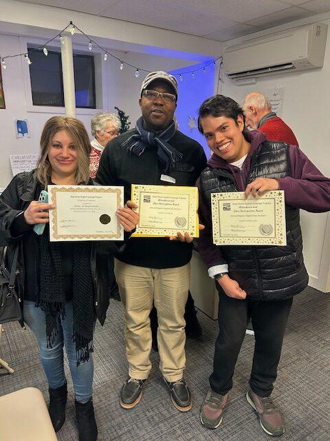 Three people stand together holding up their certificates from the English Class ceremony