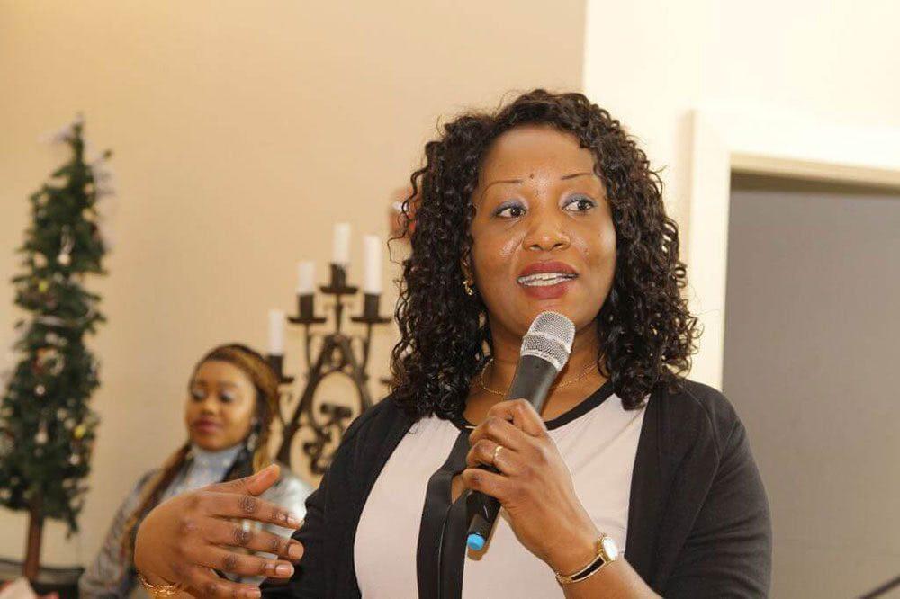 A young black woman speaks into the microphone in front of an audience.