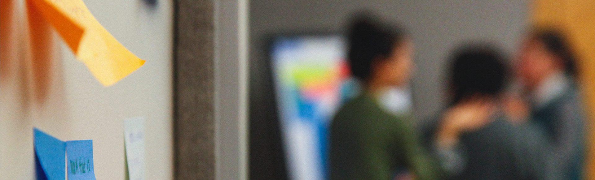 A view of educators chatting in a classroom next to a whiteboard with post-it notes stuck on it.