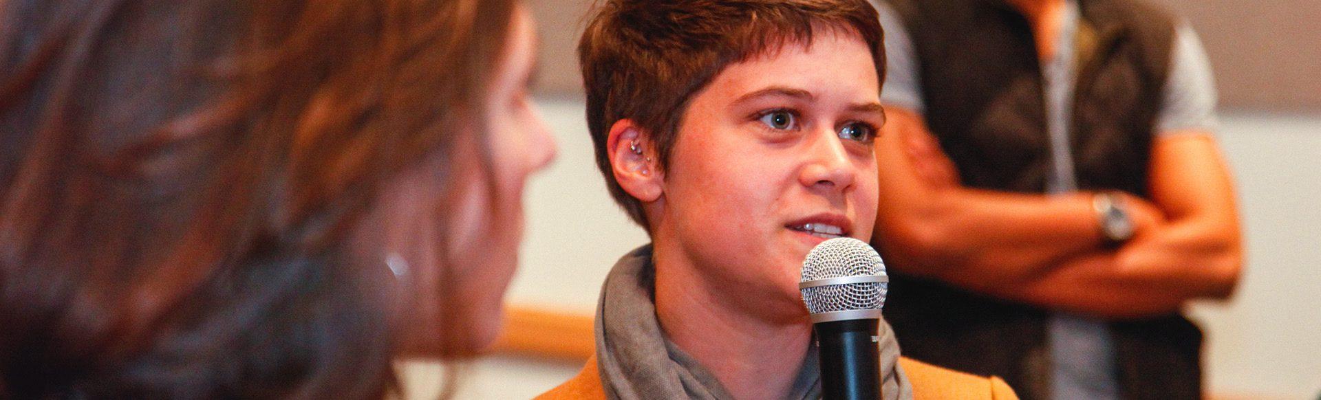 A young woman speaks into the microphone at an event