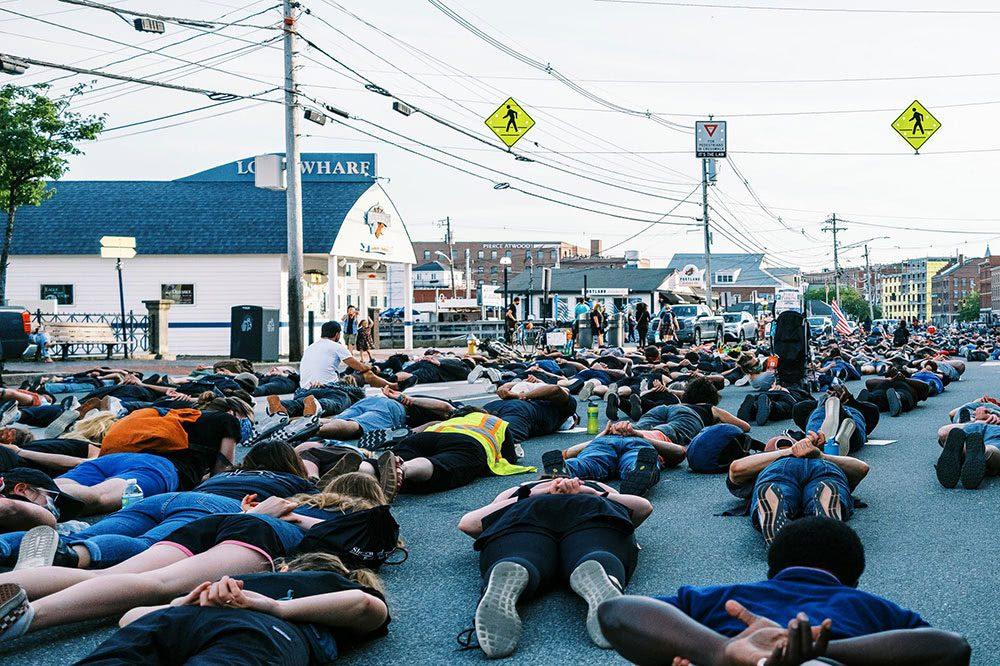 Men and women lay flat on their chests with hands behind their backs in solidarity for Black rights