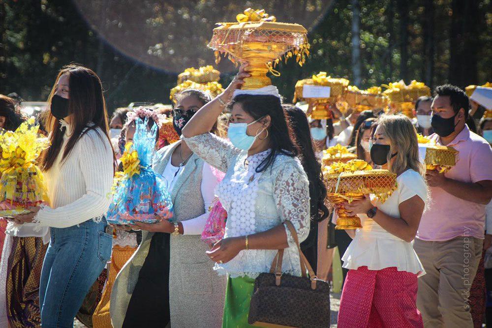Cambodian women wearing masks carry yellow, colorful, gifts