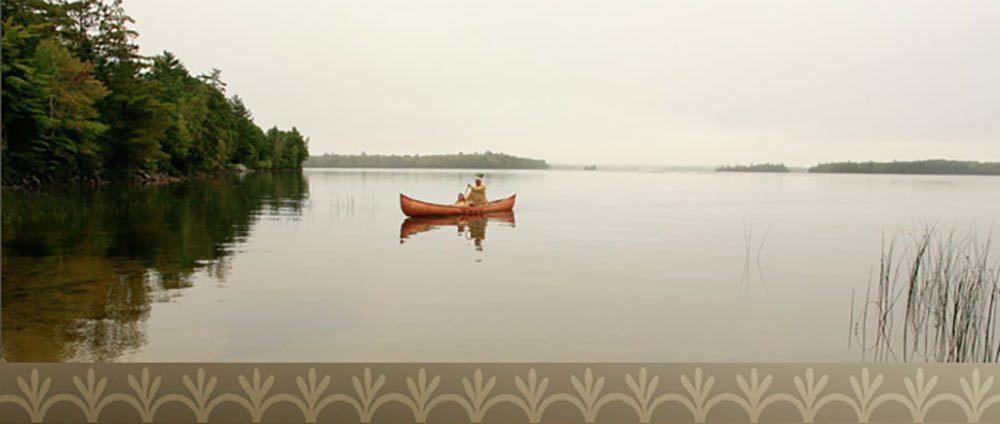 A man paddles a canoe in a serene Maine lake