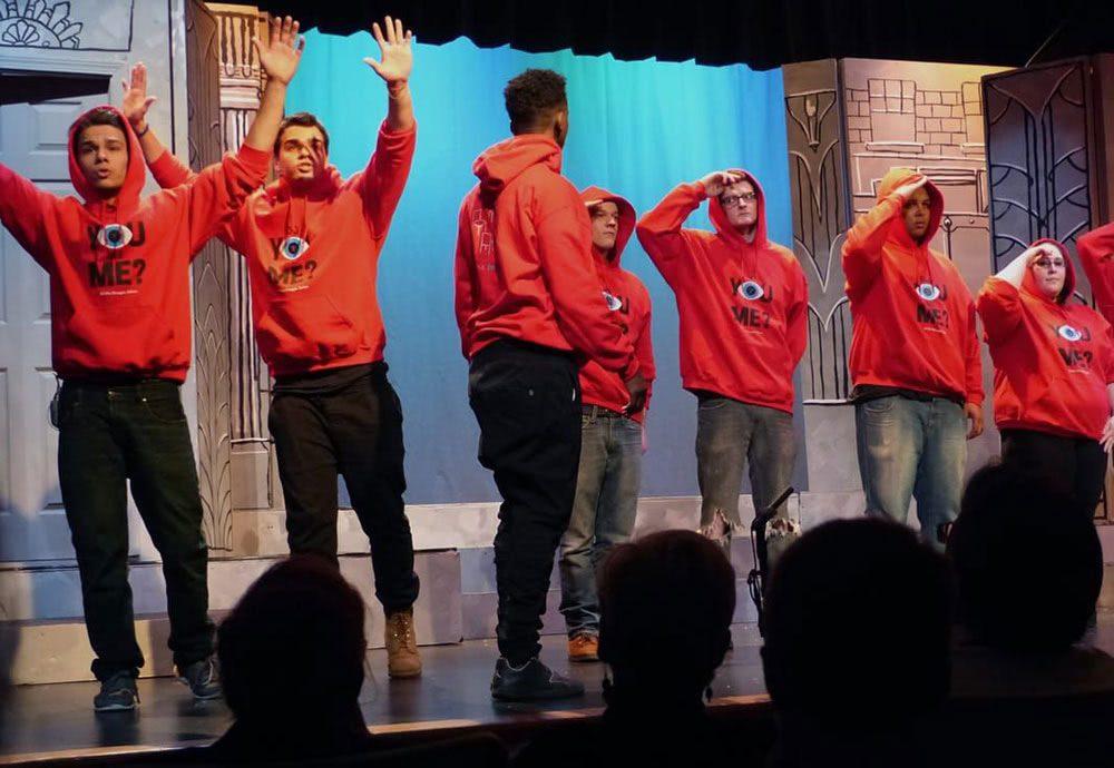 Young actors stand and pose on a stage in red sweatshirts