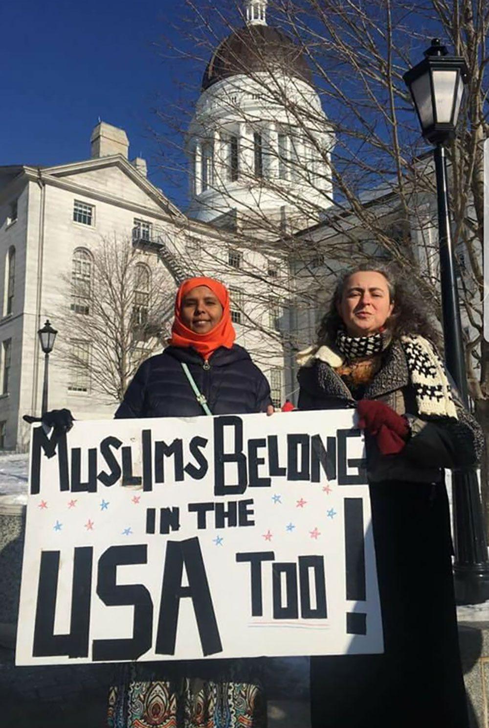Muslim women stand in front of the Maine capitol building with a protest sign