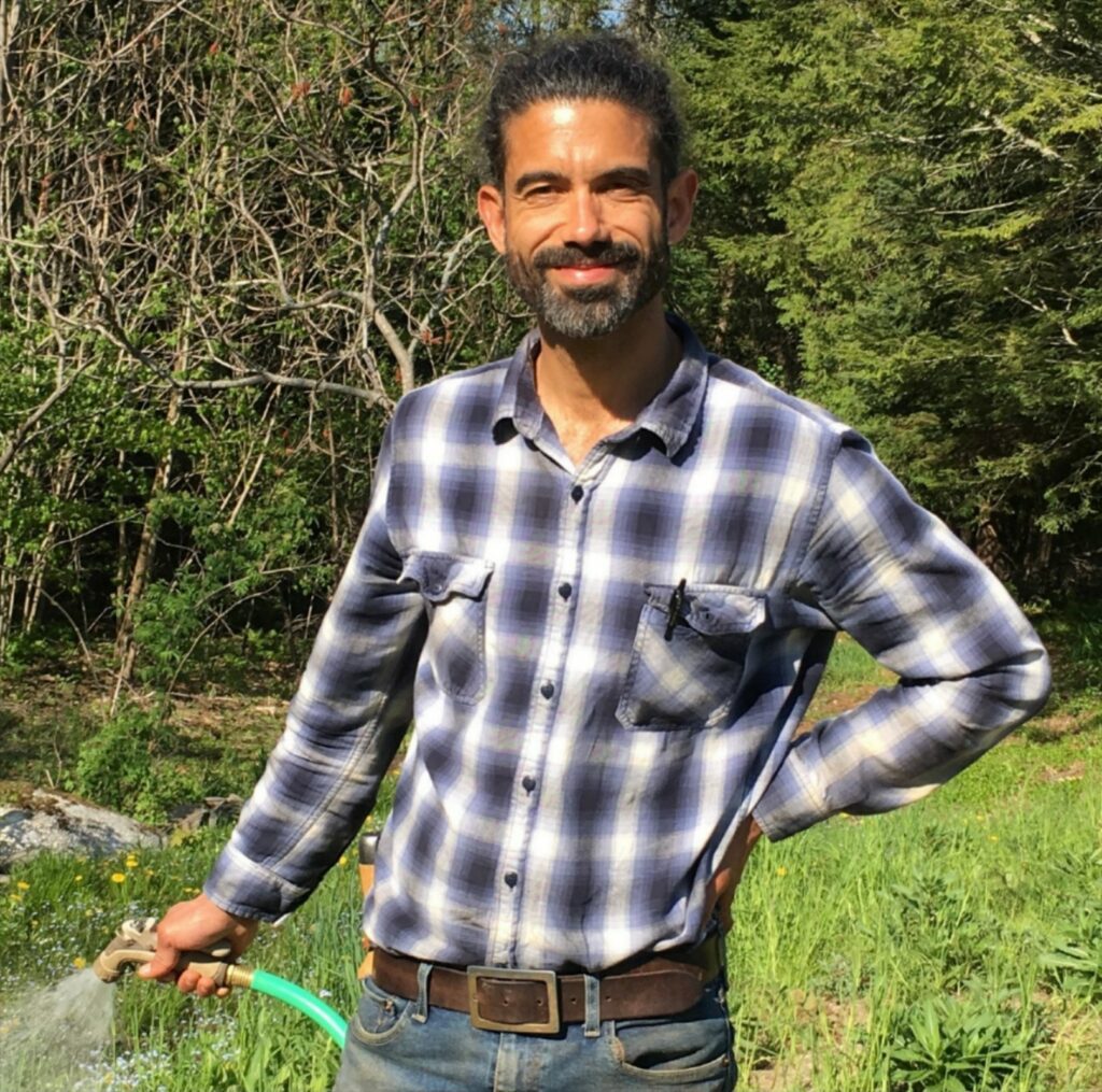 Julian Rowand poses for the camera while smiling and watering his garden