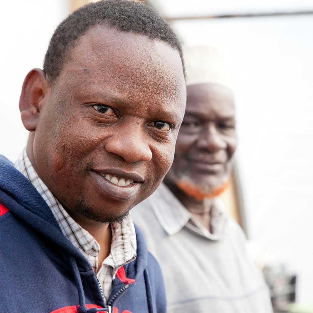 Refugee men smile for the camera in a closeup.